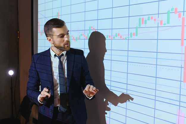 Man is standing near projector and showing graphs and business graphs