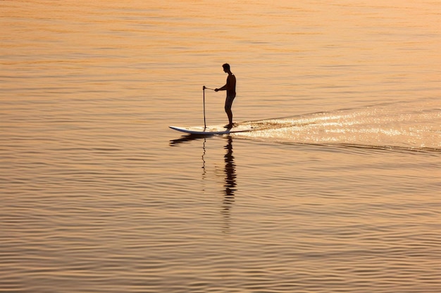 Photo a man is standing on a surfboard in the water with a paddle