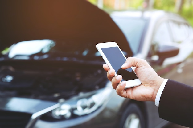 L'uomo sta usando un telefono cellulare chiama un meccanico di automobili perché l'auto era rotta