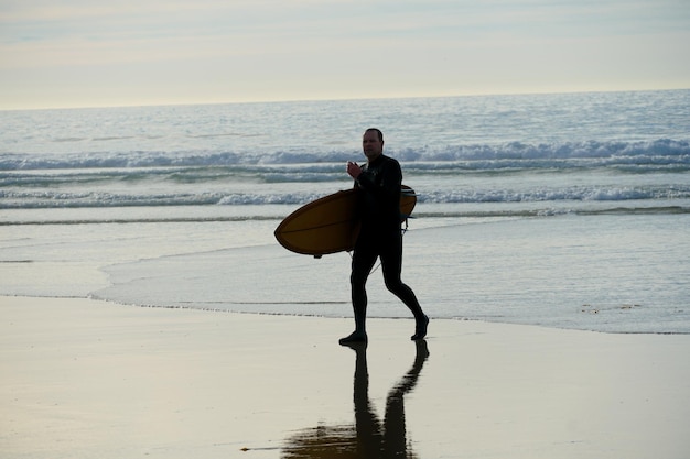 Photo a man is walking on the beach with a surfboard.