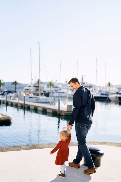 Man is walking hand in hand with his sweet 2-year old on a boat pier.  