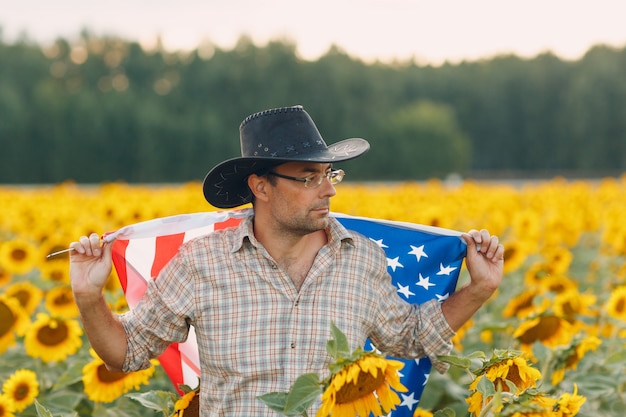 A man is walking into the sunflower field with United State flag. 4th July Independence Day concept.