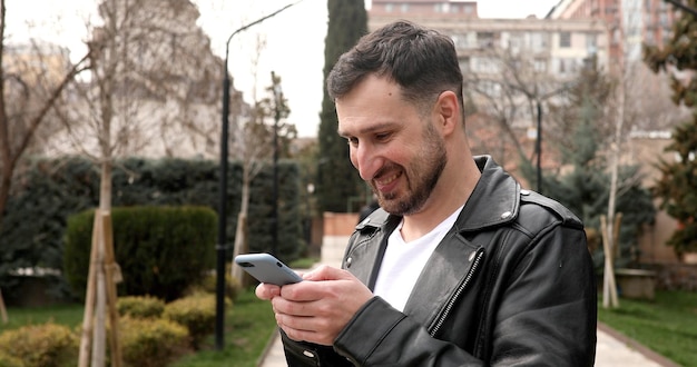 A man is wearing a black leather jacket and is looking at his phone.