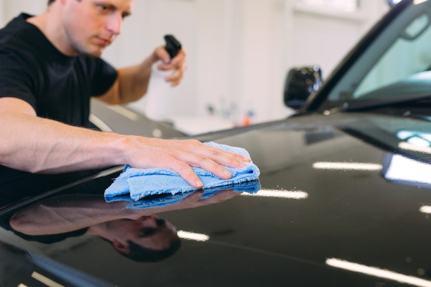 man is wiping with a cloth body of a brilliant car.