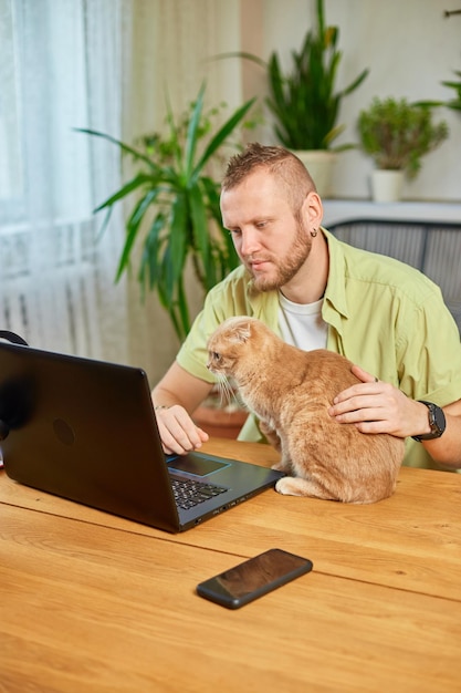 Photo man is working on a black notebook laptop and cat is laying in his hand