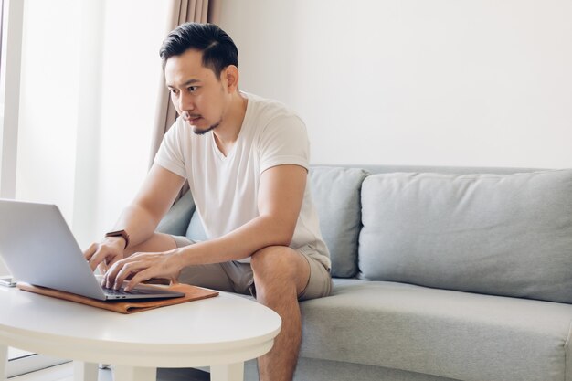 Man is working on his laptop in the living room with a cup of coffee.