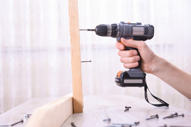 L'uomo sta lavorando con l'assemblea della mobilia facendo uso del cacciavite elettrico nell'installazione della nuova casa - lavoro in loco del tecnico facendo uso del concetto degli attrezzi per bricolage