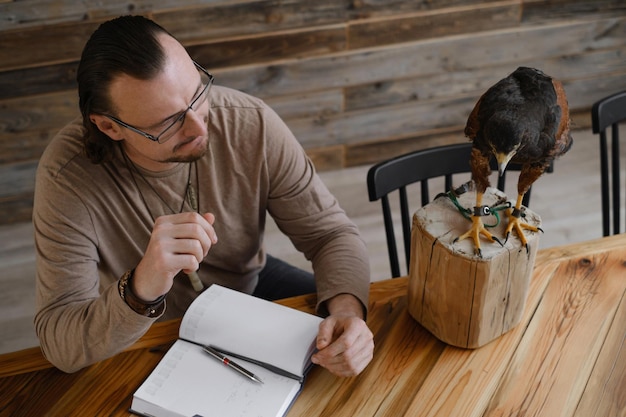 Photo man is working writing with wild bird at home by the table making noted memories diary with