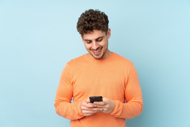 Man isolated on blue wall sending a message with the mobile