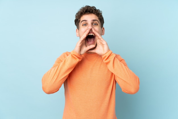 Man isolated on blue wall shouting and announcing something