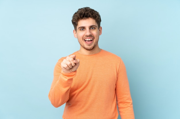 Man isolated on blue wall surprised and pointing front