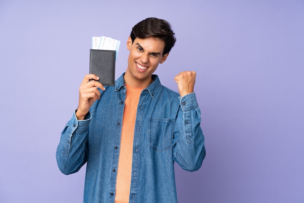 Man over isolated purple wall happy in vacation with passport and plane tickets