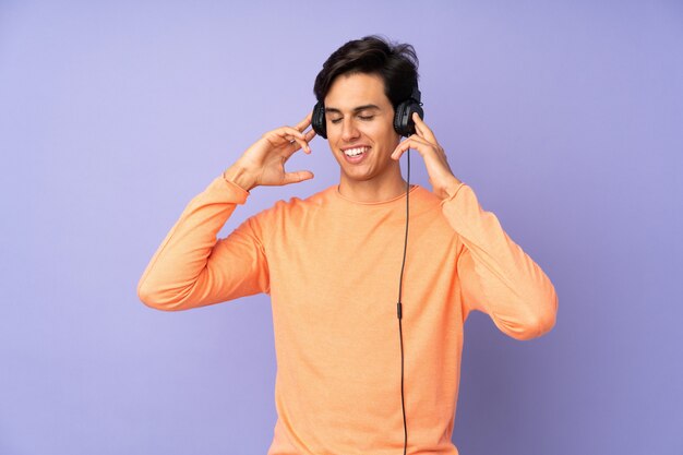 Man over isolated purple wall listening music and singing