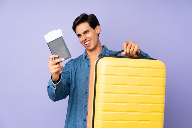 Man over isolated purple wall in vacation with suitcase and passport