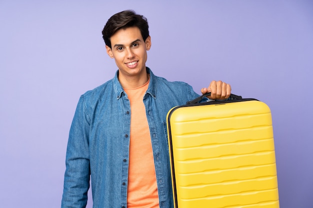 Man over isolated purple wall in vacation with travel suitcase and unhappy
