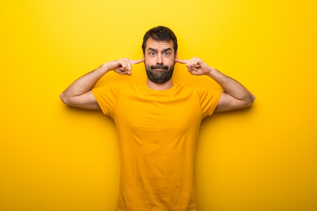 Man on isolated vibrant yellow color covering both ears with hands