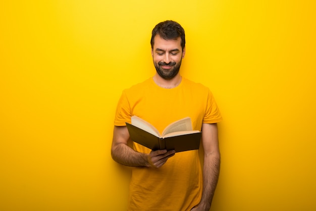 Man on isolated vibrant yellow color holding a book and enjoying reading