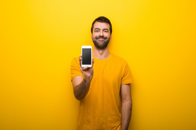 Man on isolated vibrant yellow color looking at the camera and smiling while using the mobile