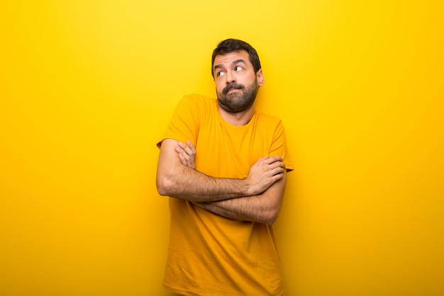 Man on isolated vibrant yellow color making doubts gesture while lifting the shoulders