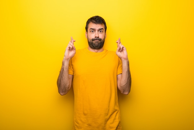 Man on isolated vibrant yellow color with fingers crossing and wishing the best