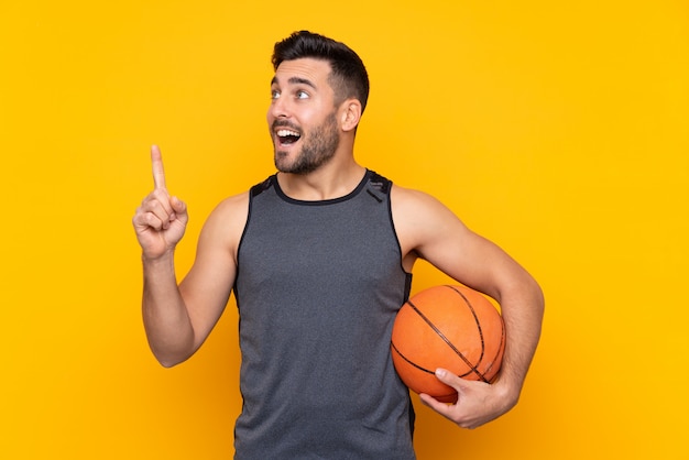 Man over isolated yellow wall playing basketball and having an idea