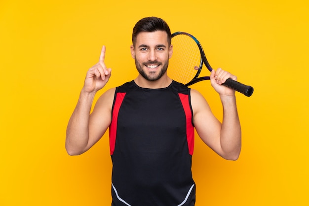 man over isolated yellow wall playing tennis and pointing up