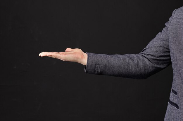 Man in a jacket holds an object in the palm of his hand on a black background.