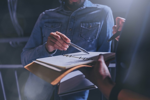 Man in jeans gives advice on work in a notebook with colleagues in office.