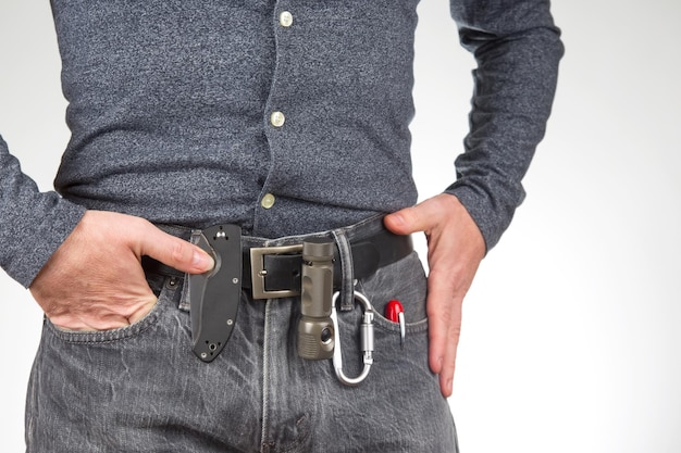 Man in jeans on a leather belt with a flashlight and a knife survival items