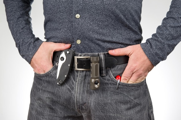 Man in jeans on a leather belt with a flashlight and a knife survival items