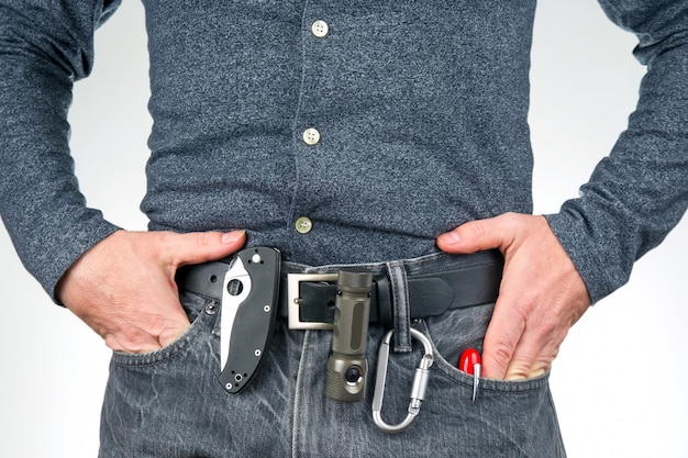 Man in jeans on a leather belt with a flashlight and a knife survival items