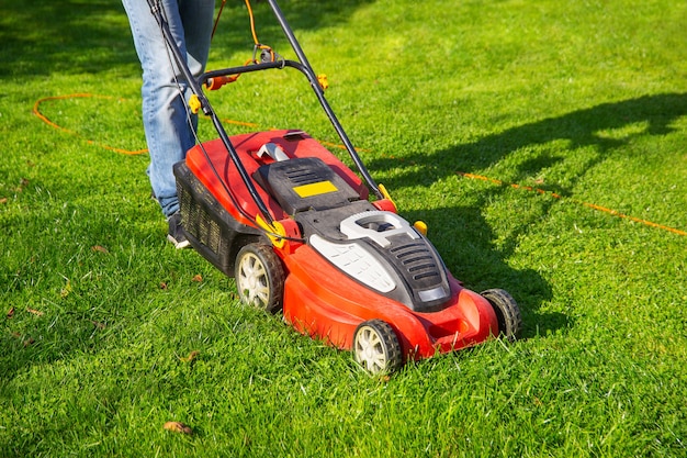 a man in jeans mows the grass in the garden with a lawn mower summer day