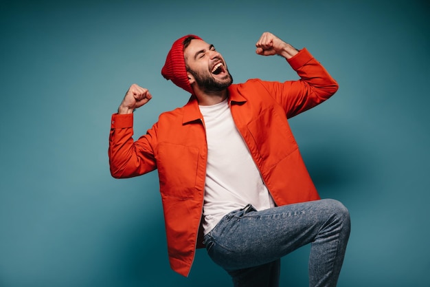 Man in jeans and orange jacket celebrates victory on blue background