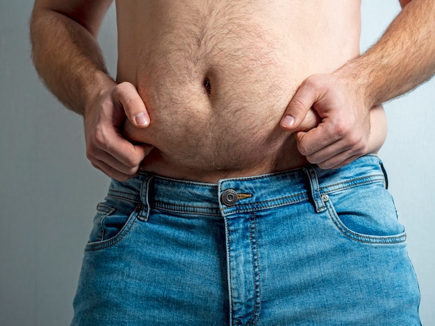 The man in jeans squeezes his hairy, flabby, fat stomach. The concept of poor nutrition. body positive. Self-acceptance