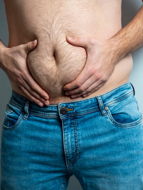 Foto l'uomo in jeans si stringe il ventre peloso, flaccido e grasso.