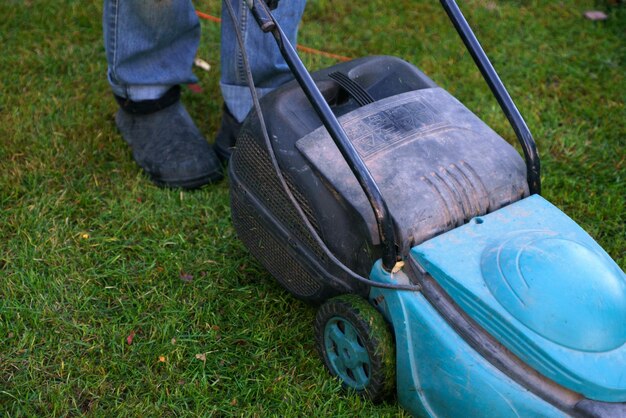 A man in jeans with a lawn mower mows a lawn strewn with fallen autumn leaves Photo from below only legs in the frame