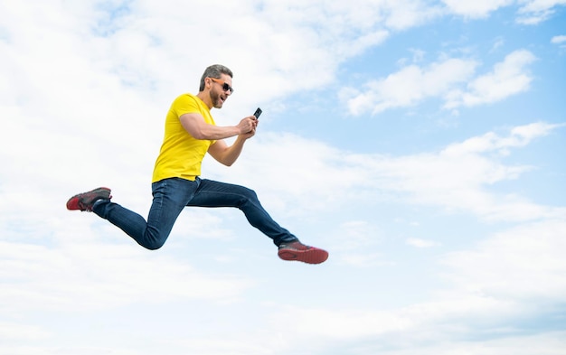 空の背景のコピースペースにスマートフォンでジャンプしてチャットする男