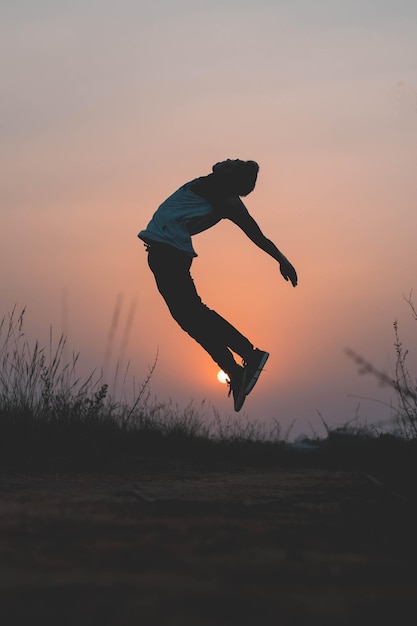 man jumping on field against sky during sunset