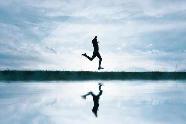 Photo man jumping in the field and reflecting in the lake