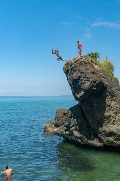 Foto l'uomo che salta da alta roccia al mare