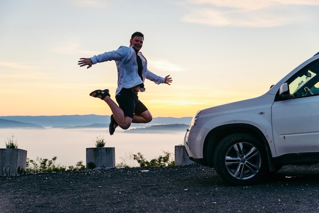 山の上の白いsuv車の日の出の近くでジャンプする男霧の天気魔法の時間