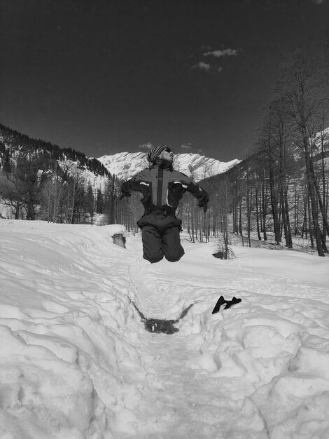 Foto uomo che salta su una terra innevata contro il cielo.