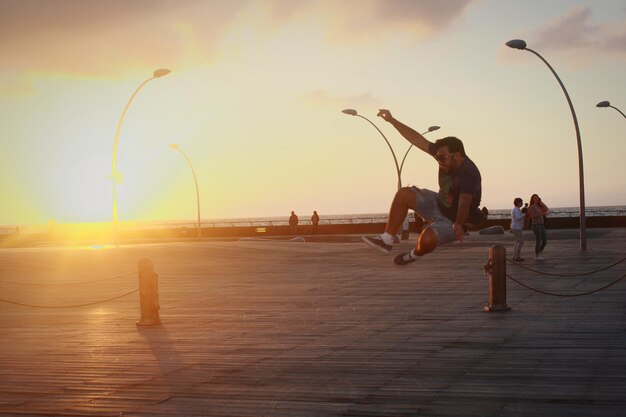 Man jumping on street against sea during sunset