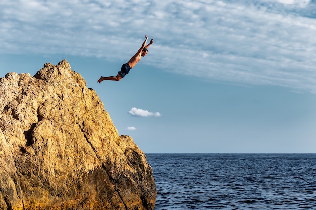 Мужчина прыгает в море с высокой скалы