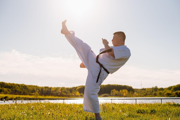 Мужчина-каратист в белом кимоно тренируется на открытом воздухе в парке