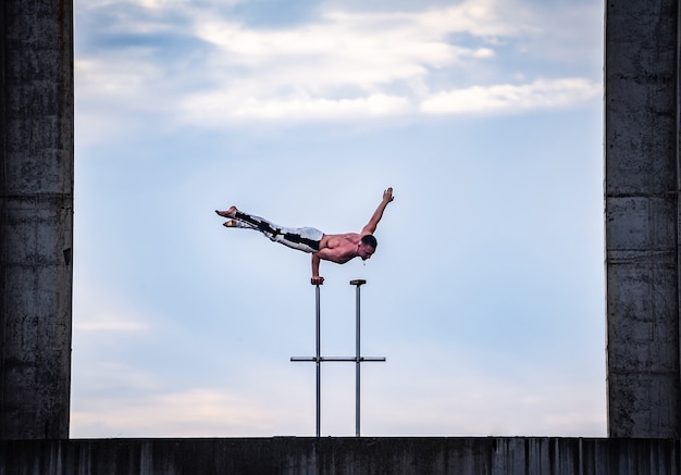 Man keeps balance on one hand on the cloudy sky background. Concept of yoga, meditation and healthy lifestyle.