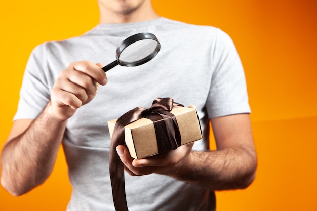 Man kijkt door een vergrootglas naar een geschenkdoos op een oranje achtergrond