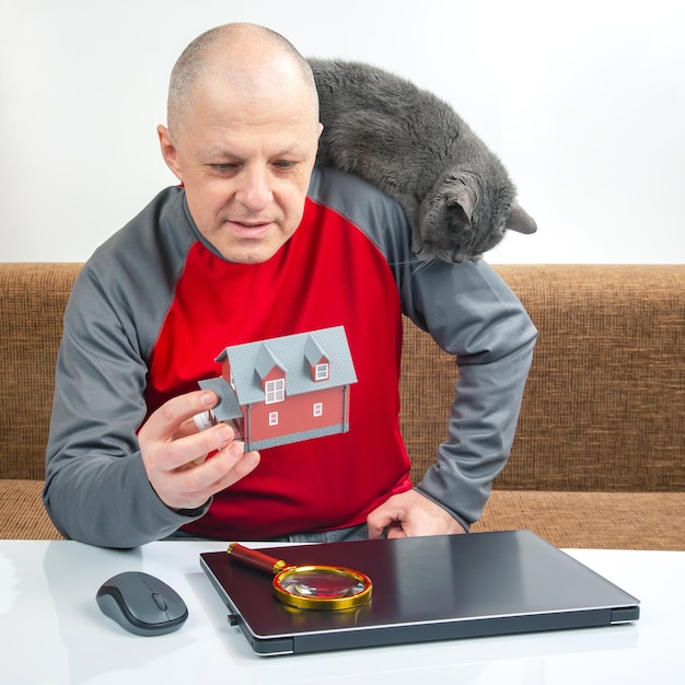 Man kijkt naar een model van een huis om online te kopen op de achtergrond van een laptop Droom van het hebben van een eigen huis Het concept van het kopen van een woongebouw