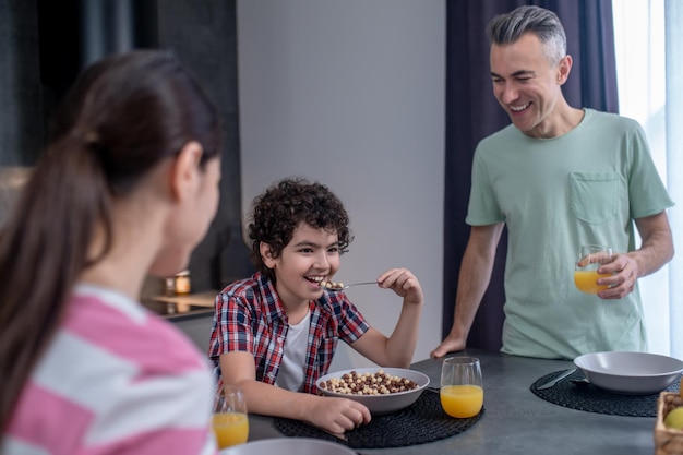 Man kijkt naar jongen die ontbijtgranen eet aan tafel