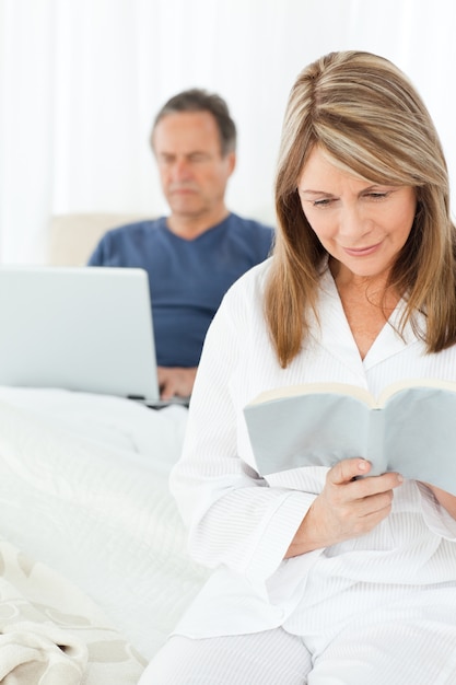 Man kijkt naar zijn laptop terwijl haar vrouw aan het lezen is